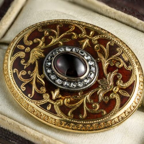 Spilla ovale in oro cesellato e smalto, nella parte centrale granato cabochon e diamanti taglio rosetta. Italia, Epoca metà' 800